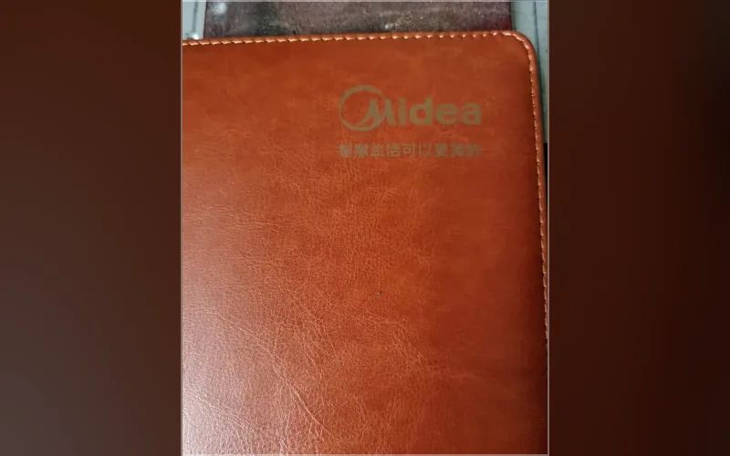 合肥激光打标代工实拍 · 棕色皮革笔记本封面激光雕刻企业 logo 与品牌标语，深浅可控批量一致